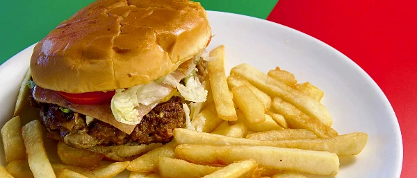 A Mexican burger on a seeded bun with lettuce and tomato, served with a pile of French fries.