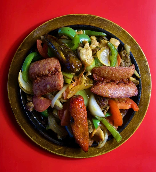 A cast-iron parrillada skillet seen from above, loaded with sausage, chicken, beef, grilled peppers and onions.