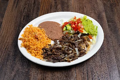 Grilled asada beef with onions on an oval plate, with Mexican rice, refried beans, pico de gallo and guacamole.