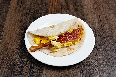 A folded flour tortilla taco filled with scrambled egg and strips of bacon.