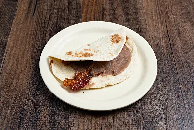 A folded flour tortilla taco filled with refried beans and bacon.