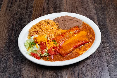 Two enchiladas covered in red chili gravy on an oval plate, with Mexican rice, refried beans and a shredded salad.