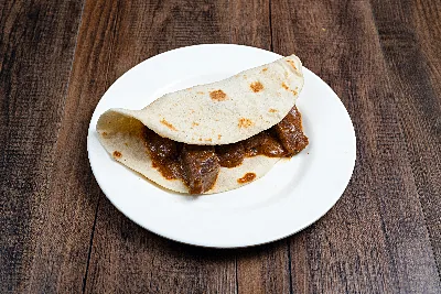 A folded flour tortilla taco filled with chunks of carne guisada in brown gravy.