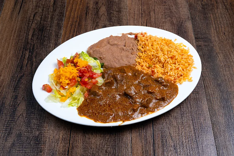 Carne guisada in its gravy with Mexican rice, refried beans and a small salad on a white plate.