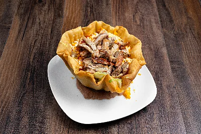 A fried tortilla bowl filled with sliced chicken fajita over lettuce, cheese and guacamole.