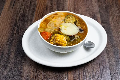 A bowl of caldo de pollo with chicken, a wheel of corn on the cob, cabbage, carrot and potato.