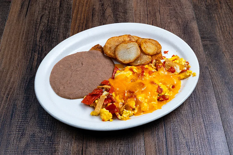 Chilaquiles under melted cheese with sliced potatoes and refried beans on an oval white plate.