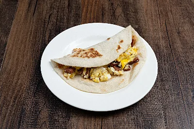 A folded flour tortilla taco filled with scrambled egg and browned country sausage.